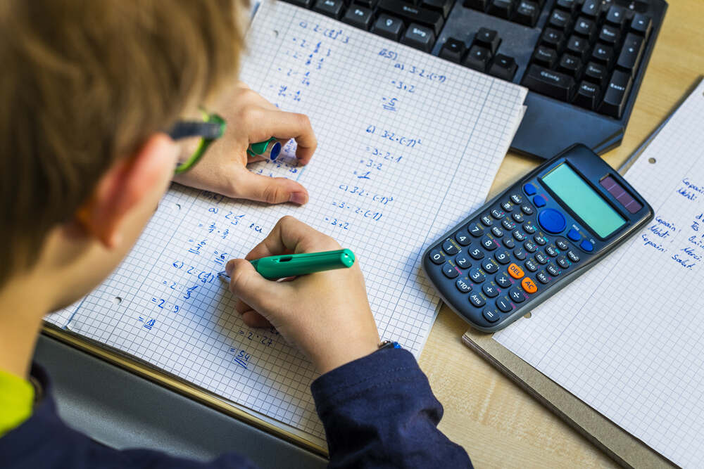 Boy writing maths with a Lamy pen in a notebook, with a calculator on his desk