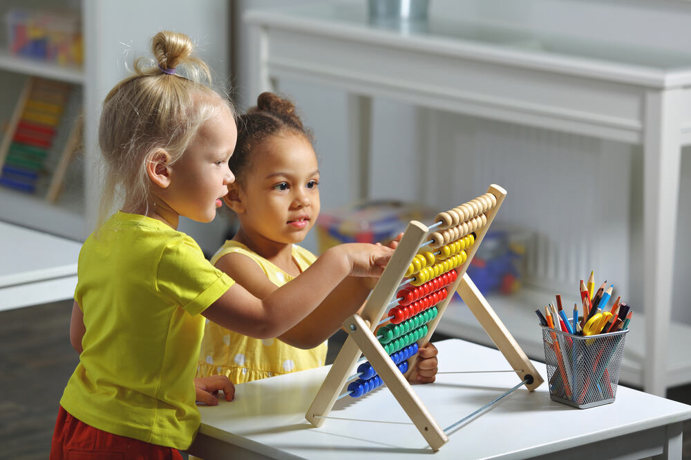 Two young girls wearing yellow playing with an abacus