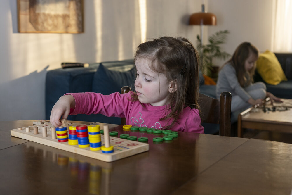 Young girl playing with counter rings with a wooden counting toy, with another girl in the background