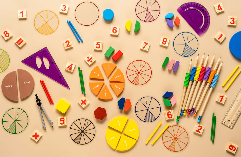 Lots of brightly coloured pencils and other stationery, colourful blocks of wood, and little number blocks on a beige table