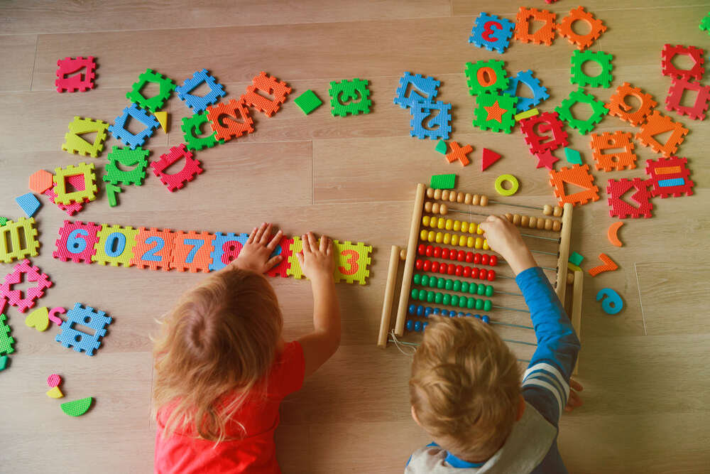 Girl and boy playing with brightly coloured foam numbers and tiles and an abacus on a wooden floor