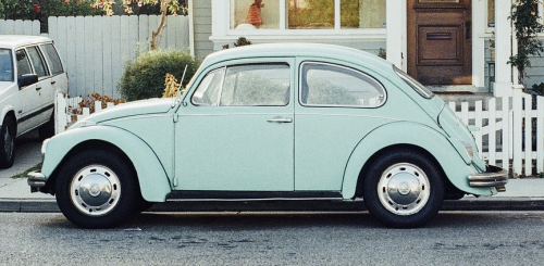 Light blue VW Beetle on the road outside a house.