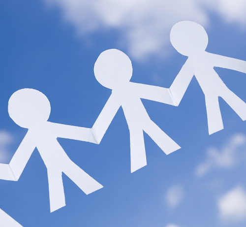 Cut out paper people with linked hands against a blue sky.