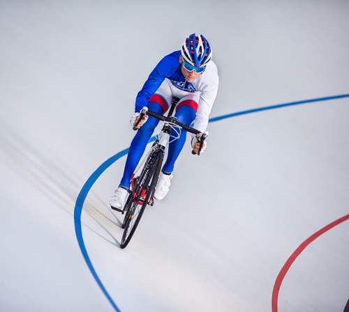 A cyclist on the curved blue line of a velodrome, which is a steeply banked track.