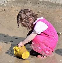 Mud Kitchen A small child gathers some wet sand into a yellow bucket.