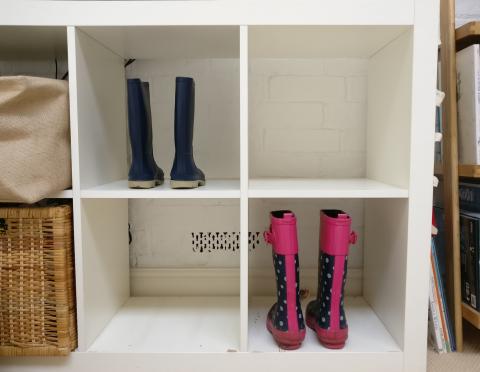 Position with Wellies A white cubby-style storage unit with six compartments. Two pairs of children's wellies are placed upright: one blue pair on the left in the top compartment and one pink and navy polka-dotted pair on the right in the lower compartment. There is a basket partially visible on the left side.