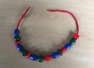 Pattern Making Small coloured beads threaded onto a red piece of string, in the pattern blue, green, red, blue, green, red, etc.
