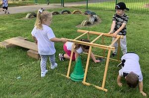 Obstacle Course Some small children are crawling through a tunnel made with sticks while two others hold the sticks to keep the tunnel secure.