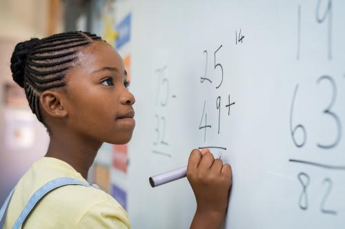 Young girl writing with a black marker on a whiteboard; close up shot of side of her face