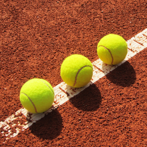 Three tennis balls on a clay surface.