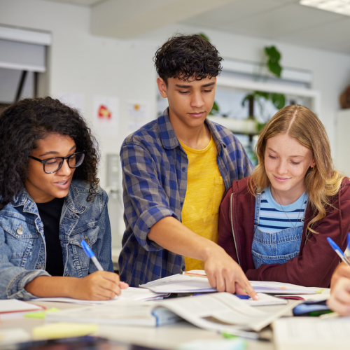 Three teenagers working together from books at a table.