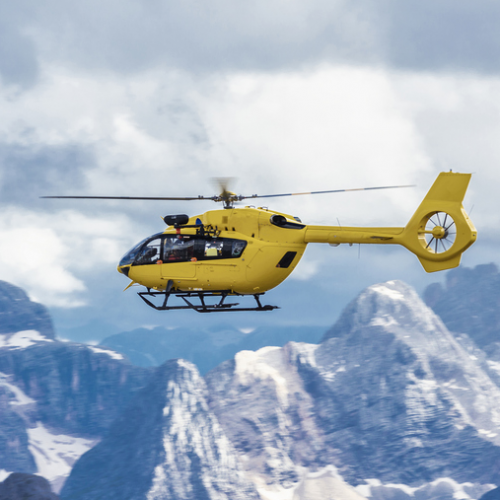 A yellow helicopter flying over the mountains.