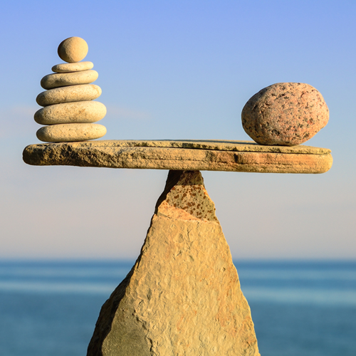 A balance scale made of rocks, with six small rocks on one side and one large rock on the other.
