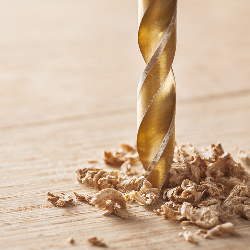 A drill making wood shavings on a block of wood.