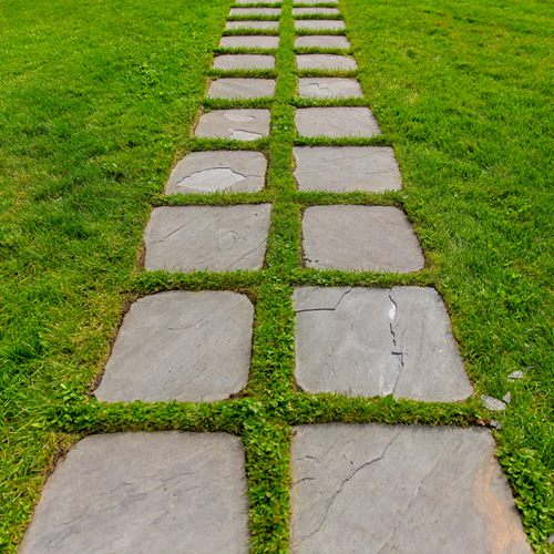 A path of square paving slabs in a green lawn.
