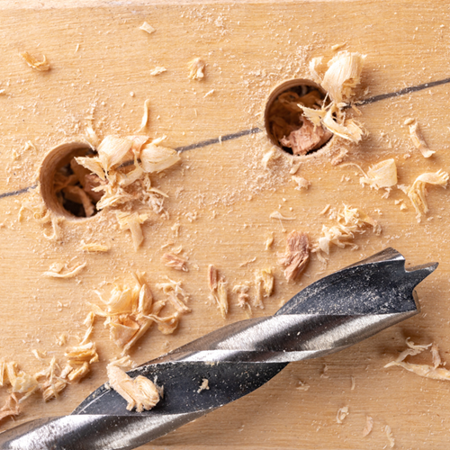 Holes drilled into wood with a drill bit beside them.