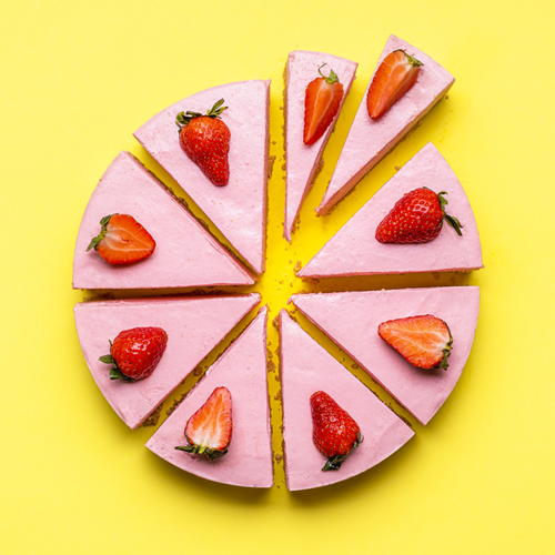 A round strawberry cheesecake cut into eighths, with one eighth cut in half.