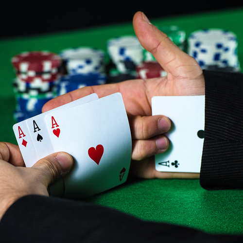 A card game player with three aces in their hand, taking a fourth ace out of their sleeve.
