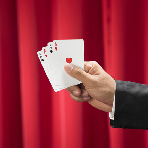 A magician holding four aces, in front of a red curtain.