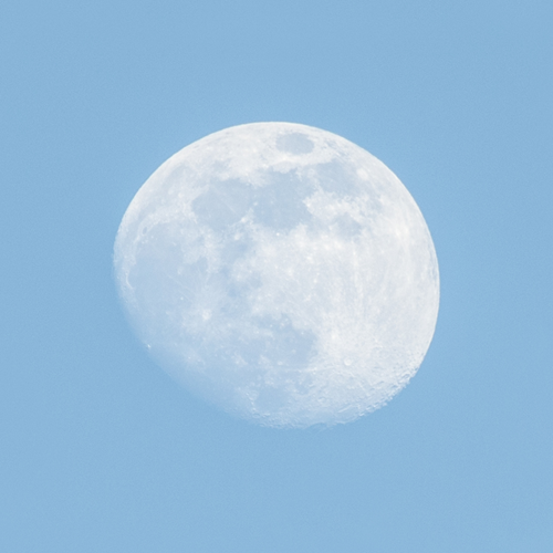 The moon during the day, against a pale blue sky.