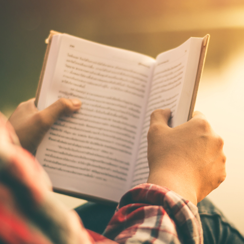 A person reading a book by a lake.