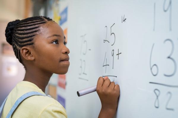 Young girl writing with a black marker on a whiteboard; close up shot of side of her face