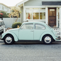 Light blue VW Beetle on the road outside a house.