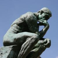 Rodin sculpture of a man thinking, his arm resting on his knee and chin resting on his hand.