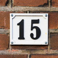 A black house number 15 on a white background, on a brick wall.
