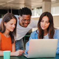 A group of teenagers looking at a laptop and smiling.