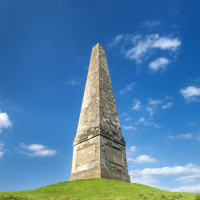 A stone obelisk on a grassy hill.