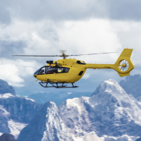 A yellow helicopter flying over the mountains.
