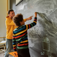 A teacher and student at a blackboard, with the student doing maths.