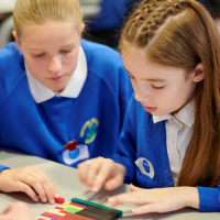 Two girls at a table moving Cuisenaire rods around.