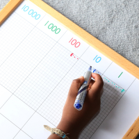A child making marks on a whiteboard showing the columns 10000, 1000, 100, 10, 1.